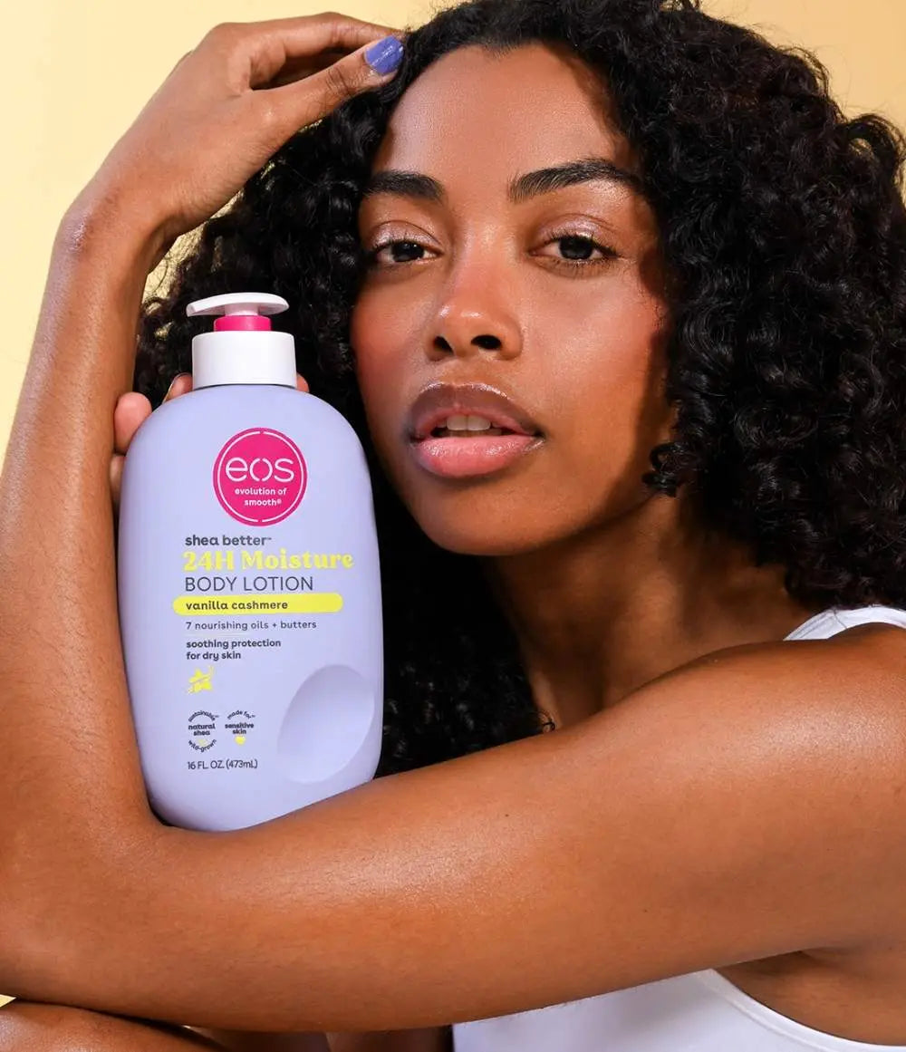 Woman holding an EOS body lotion bottle against a beige background